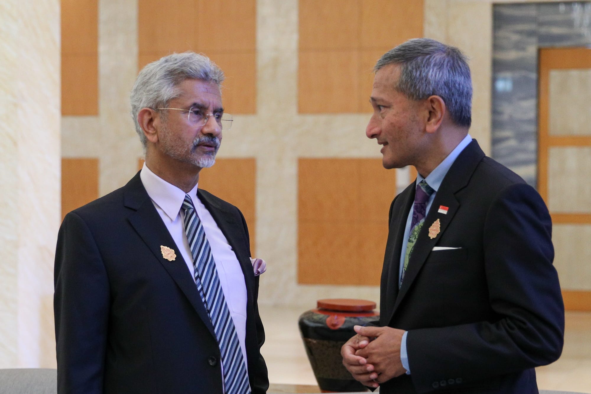 Two men in suits exchanging a book gift in a wood-paneled room.